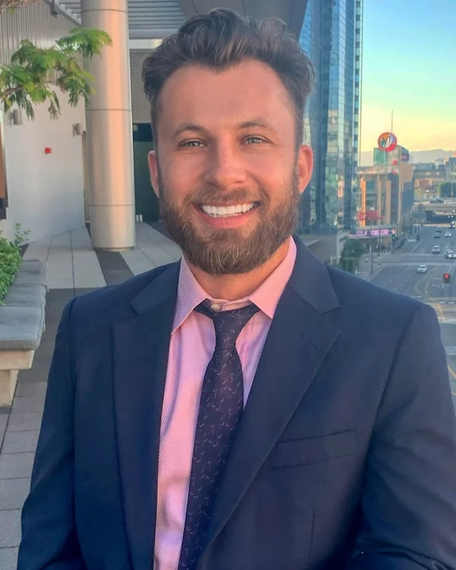 Eric Levine in a navy suit and pink shirt on a rooftop terrace.